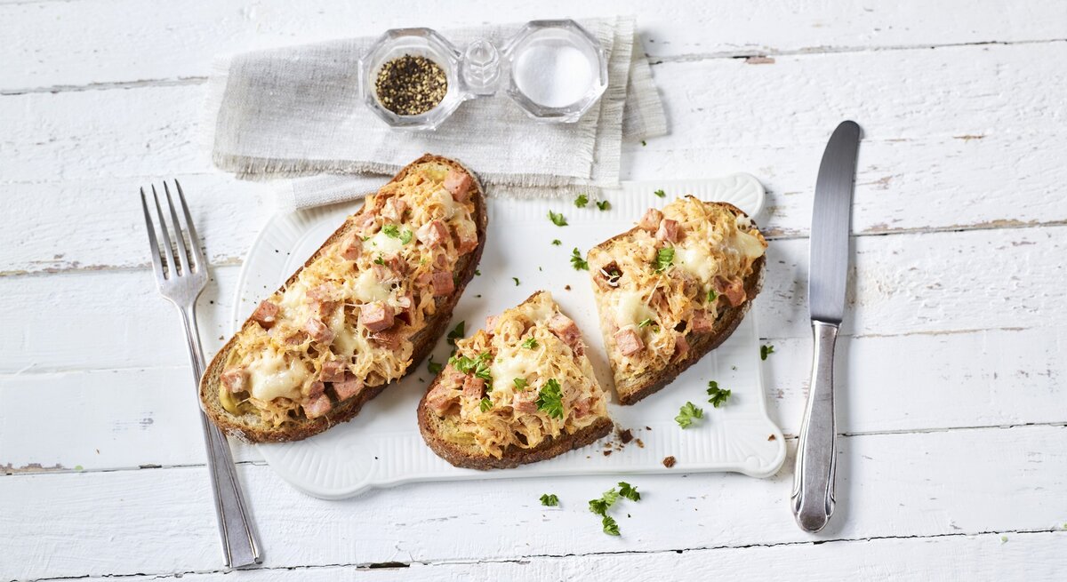 Ein weißer Holztisch mit den beiden belegten Brotscheiben von oben fotografiert.