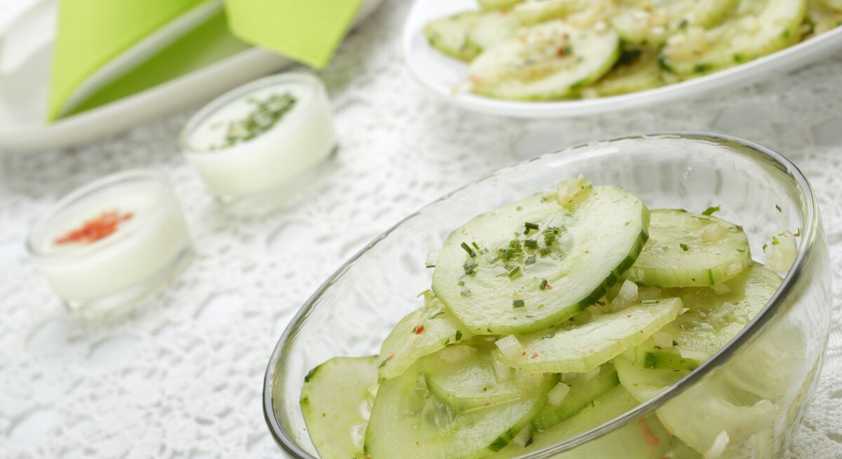 Schräge Seitenansicht auf eine Glasschale mit Gurkensalat mit durchsichtigem Dressing. 