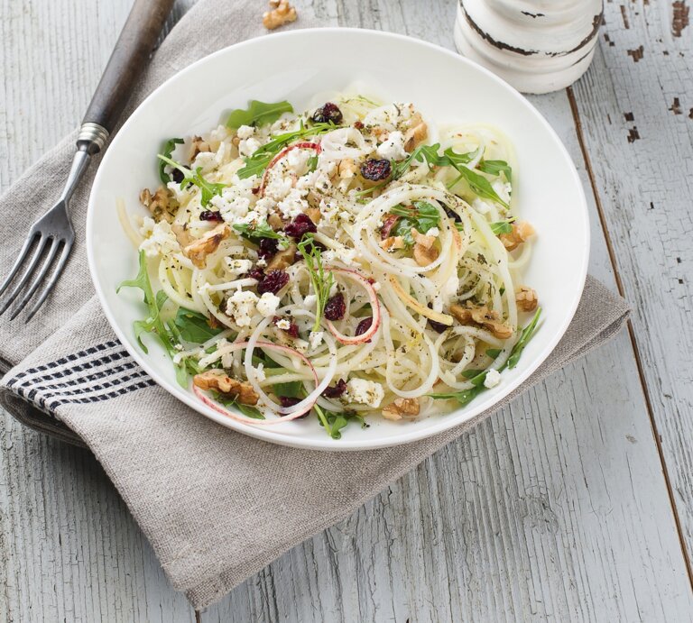 Draufsicht: Ein runder Teller mit einem Kohlrabi-Apfel-Salat mit Käse und Walnüssen auf einem hellen Untergrund aus Holz. | © StockFood/Schall, Ewgenija