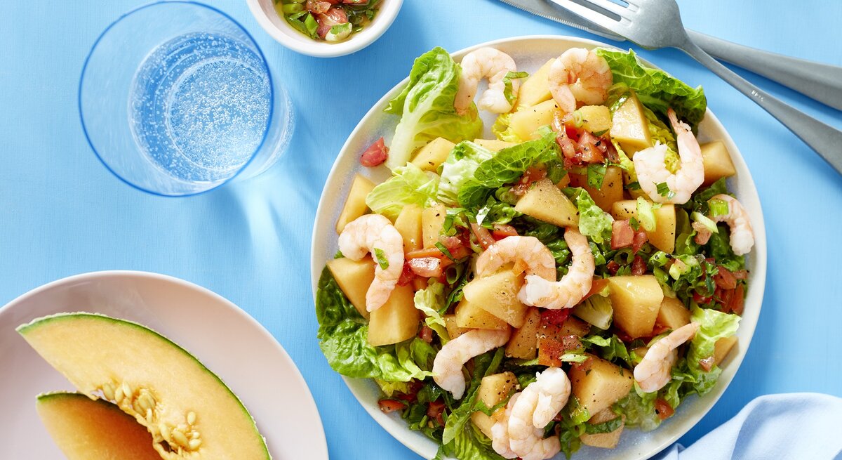 Melonensalat mit Garnelen auf weißen Tellern auf blauem Hintergrund.