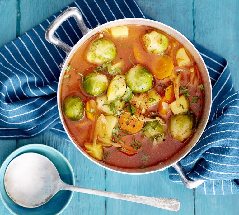 Rosenkohl-Kartoffel-Eintopf auf einem blauen Geschirrtuch auf blauem Hintergrund. Links unten auf dem Foto eine Schöpfkelle.  | © Eat Club/Isabell Triemer