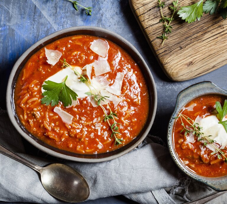 Tomatensuppe mit Reis, Hackfleisch und Parmesanspänen in einer grauen Schale auf einem dunkelblauen Steintisch. Alles direkt von oben fotografiert. | © StockFood/Brooks-Dammann, Susan