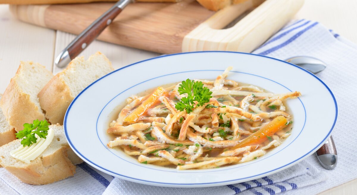 Blau-weißer Teller gefüllt mit Flädlesuppe auf einem blau-weißen Tuch. 