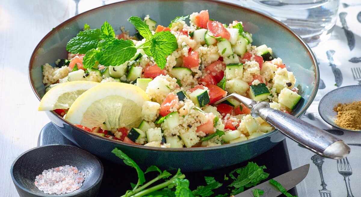 Couscous-Zucchini-Pfanne in einer blauen Schüssel. Auf dem Foto verteilt Salz, Gewürze, ein Messer und Wasser.