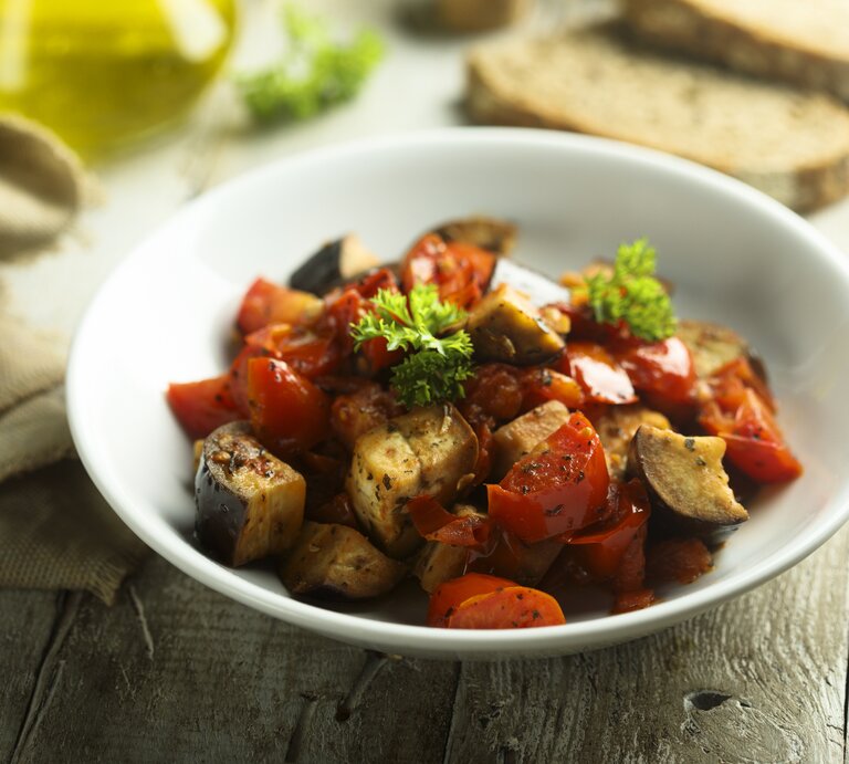 Italienischer Auberginen-Eintopf Caponata in weißem Teller auf rustikaler Oberfläche. | © iStock.com/Mariha-kitchen