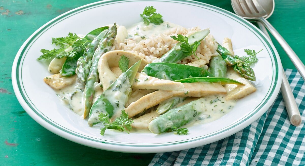 Teller mit Tofu-Geschnetzeltem, grünem Spargel und cremiger Soße.