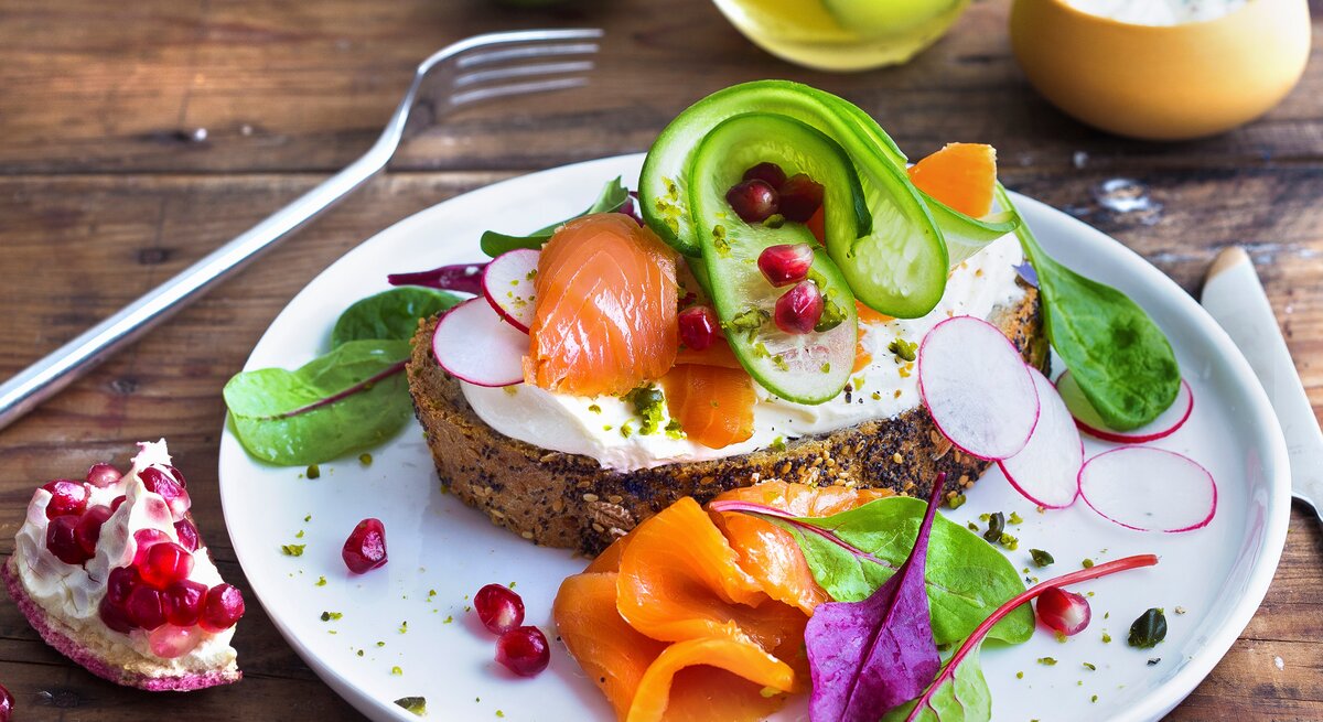 Draufsicht, schräg: Ein weißer Teller mit einer Low-Carb-Stulle mit Lachs und Pistazien.
