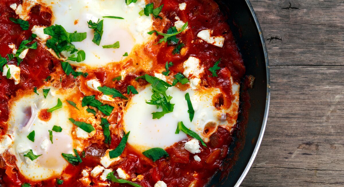 Draufsicht auf eine runde Pfanne gefüllt mit Gemüse und Ei, auch Shakshuka genannt,
