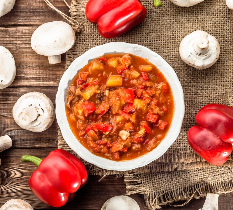 Ungarischer Eintopf mit Hackfleisch & Paprika auf rundem Teller, der auf einem Holztisch steht. | © iStock/ alicjane