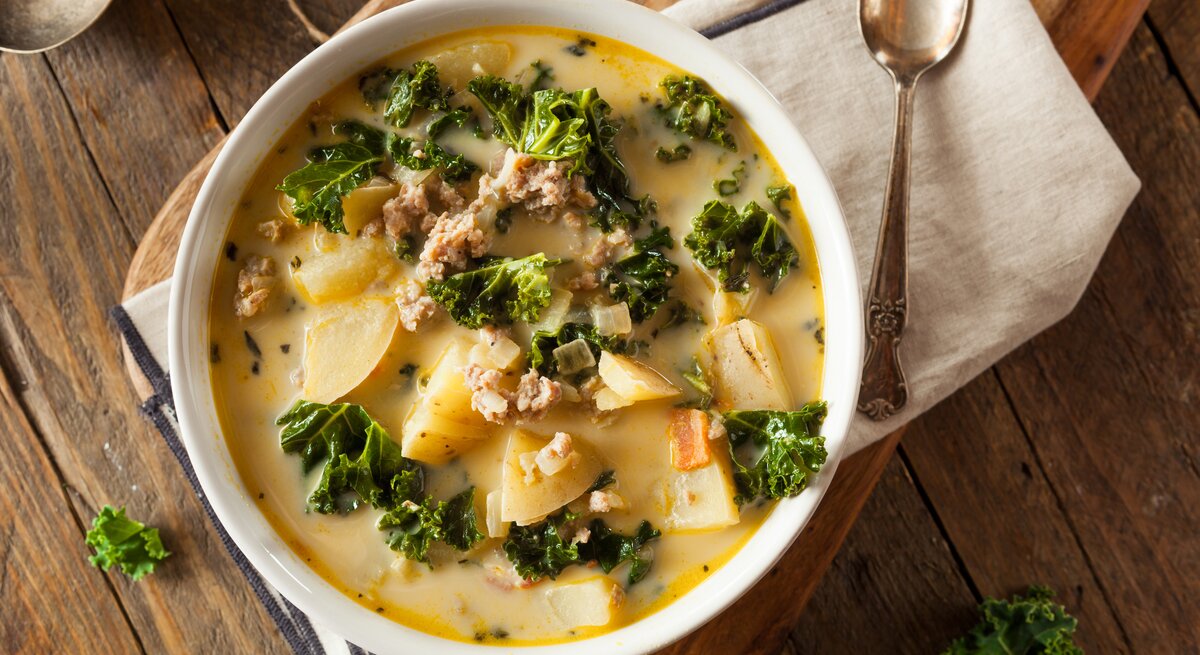 Kartoffelsuppe mit Grünkohl und Hackfleisch in weißer Schüssel auf Holz.