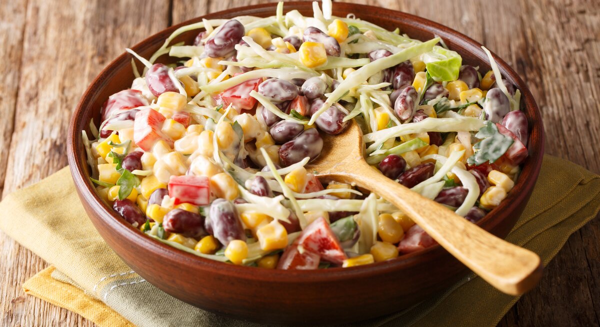 Bunter Bohnensalat mit Mais, Tomaten und Kohl in einer hölzernen Schüssel auf rustikalem Tisch.