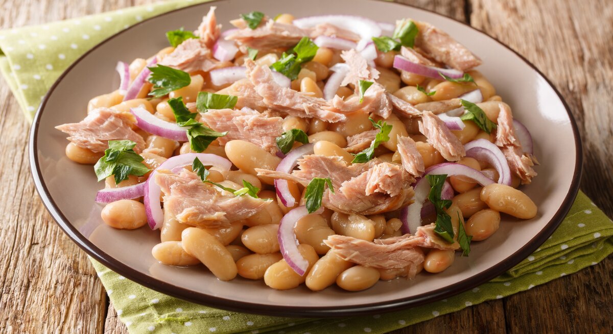 Bohnensalat mit Thunfisch und Zwiebeln auf einem Teller, angerichtet auf hölzernem Untergrund.