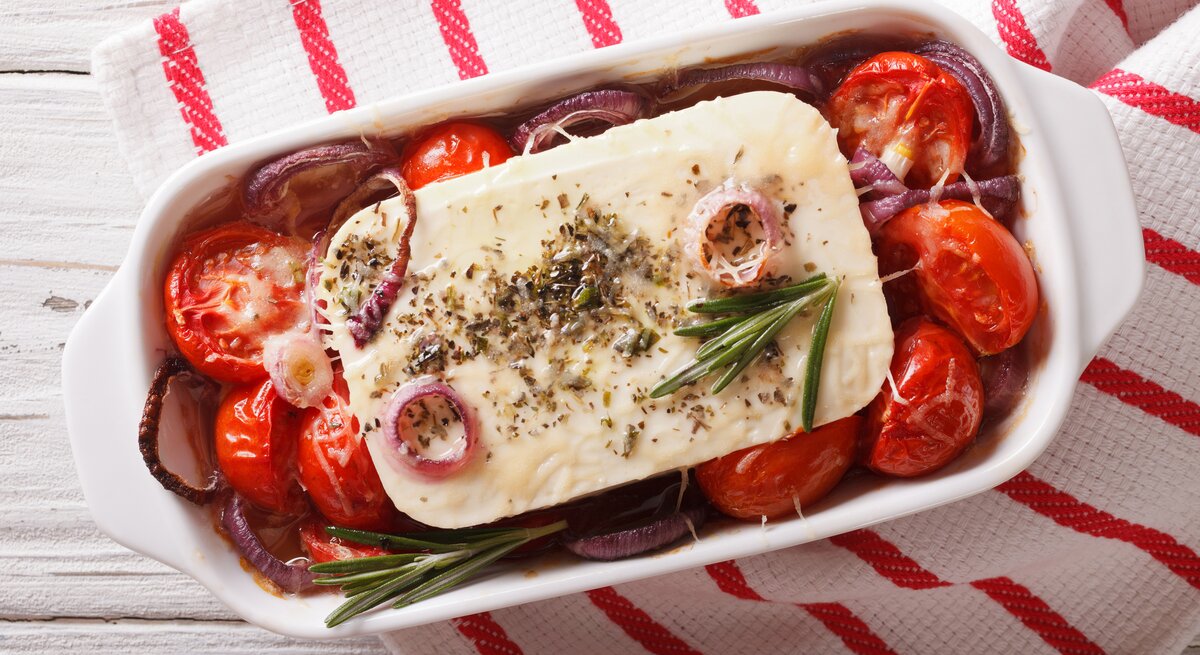 Draufsicht auf eine Auflaufform gefüllt mit gebackenem Feta, Tomaten, Rosmarin und roten Zwiebeln. 