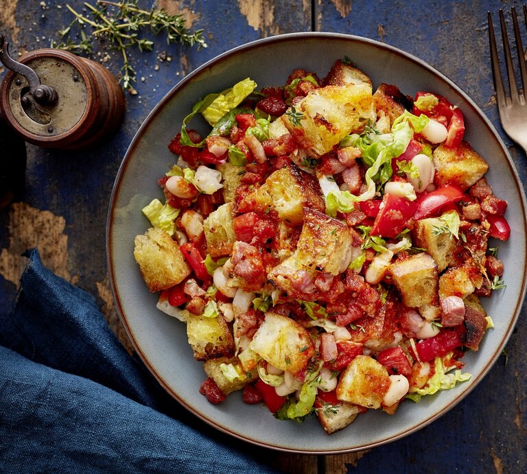 Ein grauer Teller mit dem Brotsalat mit Bohnen und Paprika auf dunkelblauem Holztisch direkt von oben fotografiert. | © Eat Club; Isabell Triemer