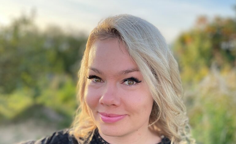 Blonde, junge Frau lächelt in die Kamera. Sie trägt ein schwarzes Oberteil und steht im Freien. Im Hintergrund erkennt man verschwommen Bäume. Madeleine Liedke ist Online-Redakteurin bei BILD der FRAU.  | © Anne Zeidler 
