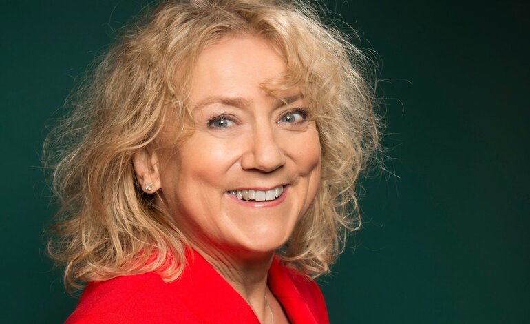Das Bild zeigt eine strahlende Frau mit lockigen blonden Haaren, die in die Kamera lächelt. Sie trägt einen leuchtend roten Blazer, der einen fröhlichen und energischen Eindruck macht. | © batchfield