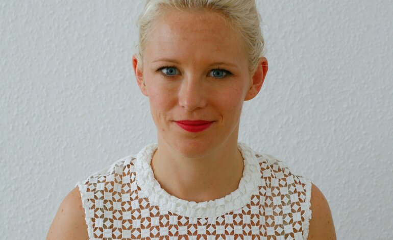 Blonde Frau mit rotem Lippenstift in weißem Shirt lächelt in die Kamera.  | © privat