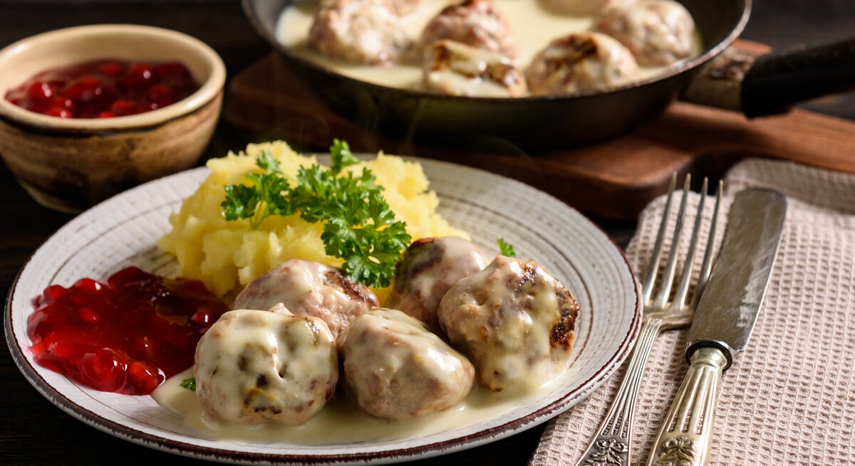 Rustikaler Teller mit Kartoffeln, Preiselbeersoße, Hackbällchen "Köttbullar" und cremiger Soße. 