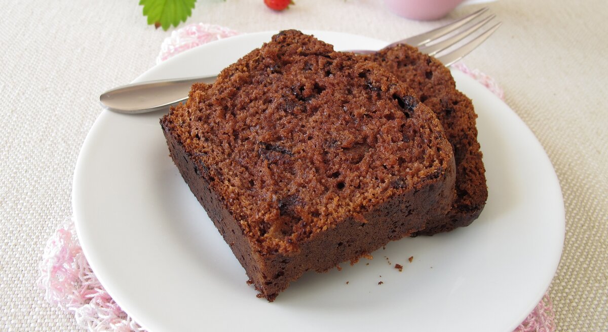 Zwei angeschnittene Stücke Schokoladenkuchen liegen auf einem weißen Teller. Daneben eine rosafarbene Tasse und ein Minzblatt. 