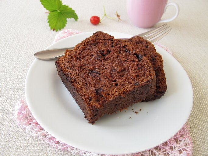 Zwei angeschnittene Stücke Schokoladenkuchen liegen auf einem weißen Teller. Daneben eine rosafarbene Tasse und ein Minzblatt.  | © iStock.com/HeikeRau