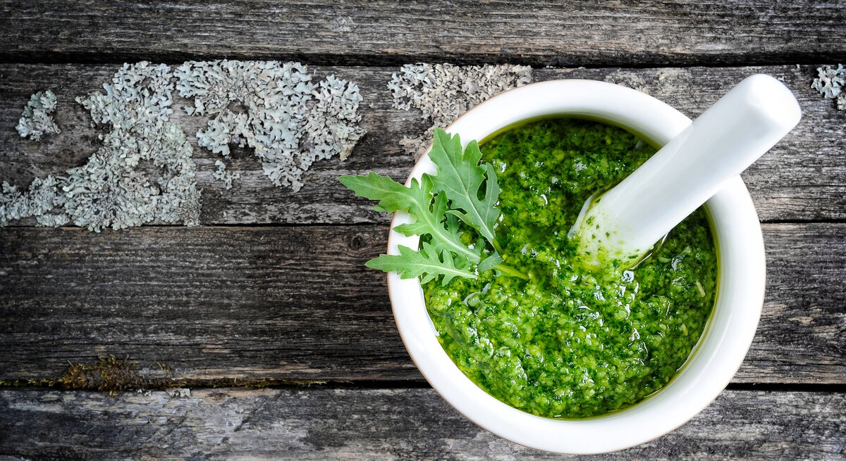 Weiße Schale gefüllt mit Rucola-Pesto auf grauer Holz-Oberfläche. 