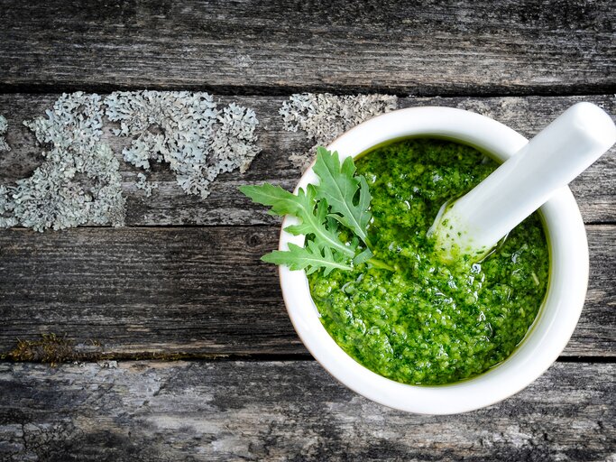 Weiße Schale gefüllt mit Rucola-Pesto auf grauer Holz-Oberfläche.  | © iStock/count_kert
