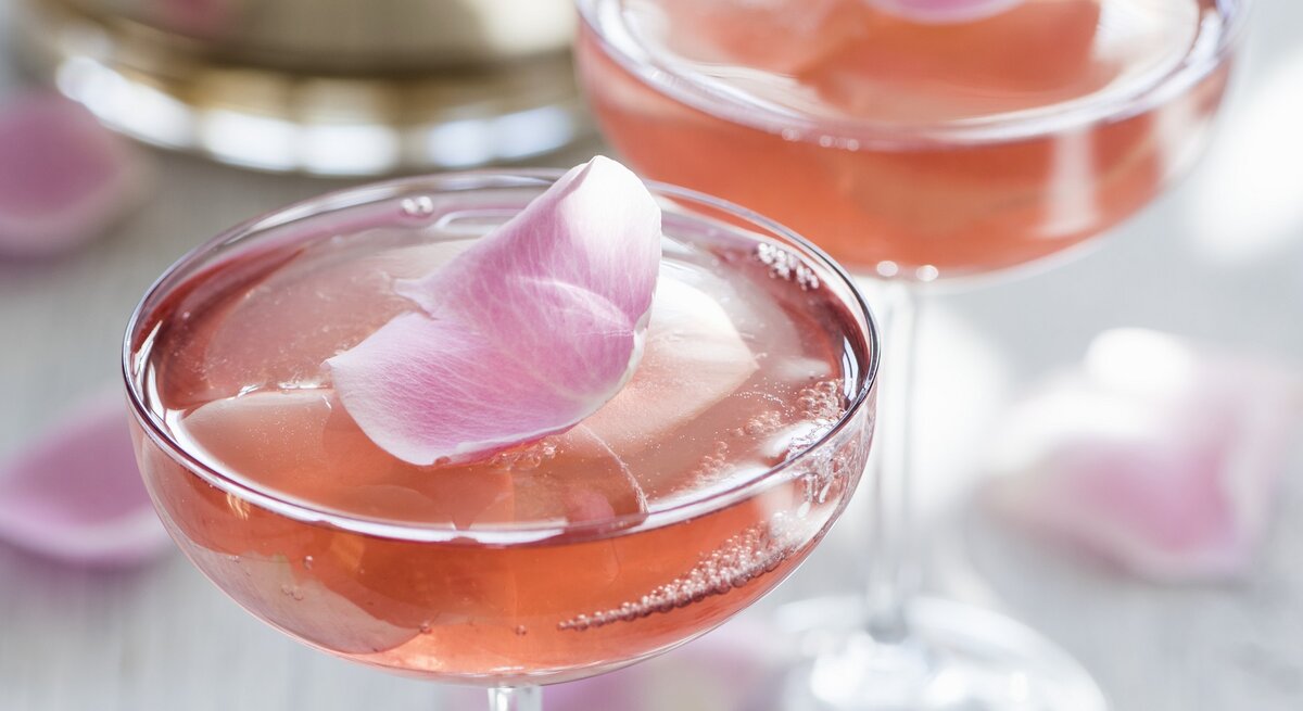 Zwei Champagnergläser mit rosa Sektgelee, in denen essbare Rosenblätter eingeschlossen sind.