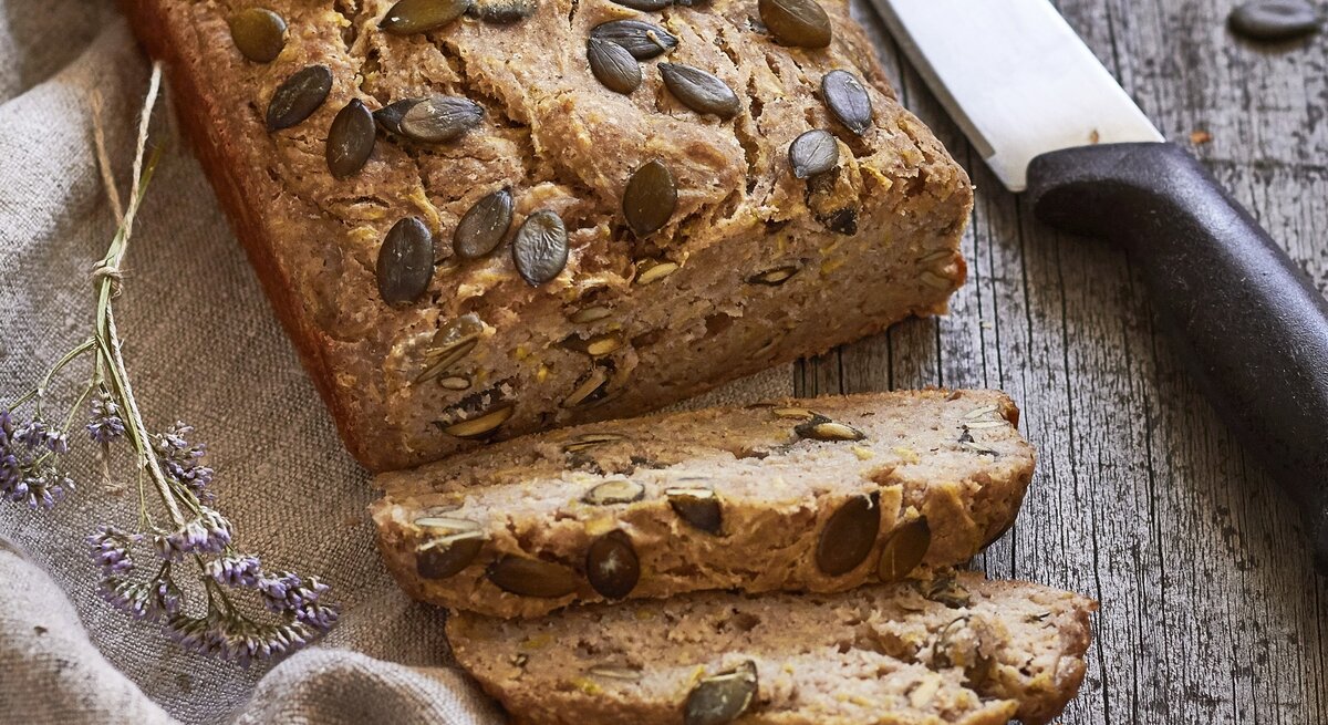 Ein angeschnittenes Zucchinibrot mit Banane. Daneben liegt ein großes Küchenmesser.