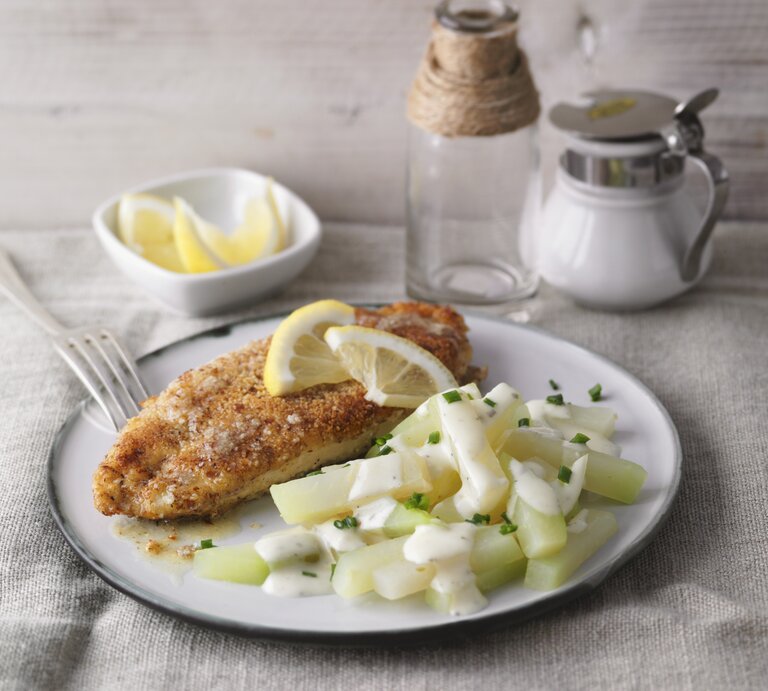 Ein weißer Teller mit dem Mandel-Schnitzel und Kohlrabi-Rahm auf einem hellen Tisch mit Zitronenecken garniert. | © StockFood / Gräfe & Unzer Verlag / Kramp + Gölling
