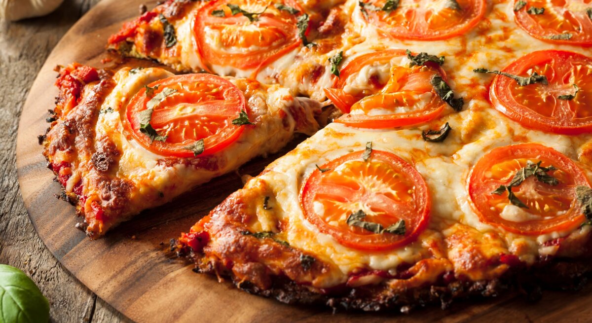Nahaufnahme der Blumenkohl-Pizza auf einem rustikalen Holztisch mit Tomaten und Basilikum.