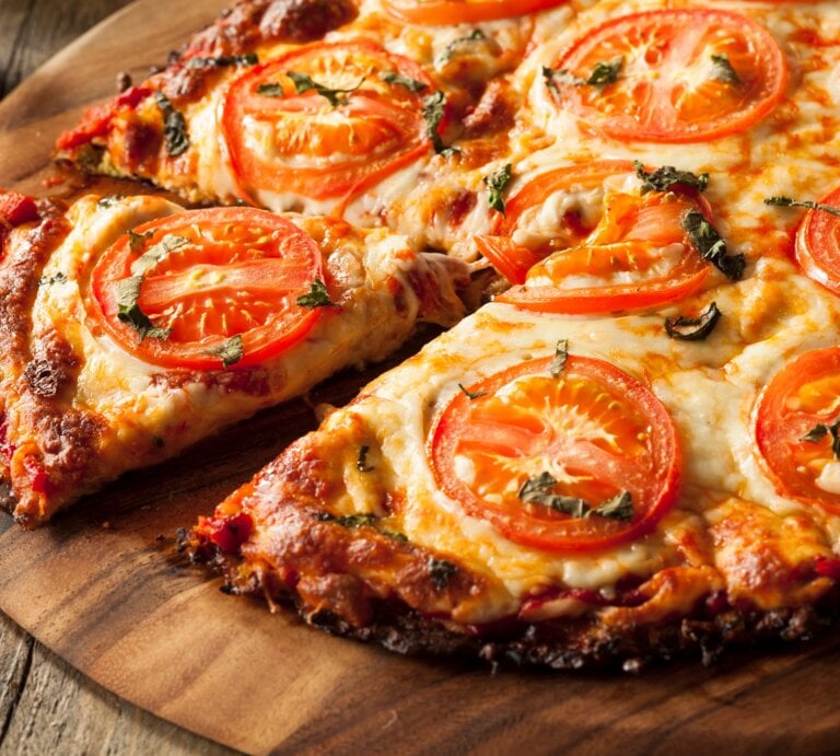 Nahaufnahme der Blumenkohl-Pizza auf einem rustikalen Holztisch mit Tomaten und Basilikum. | © istock/bhofack2