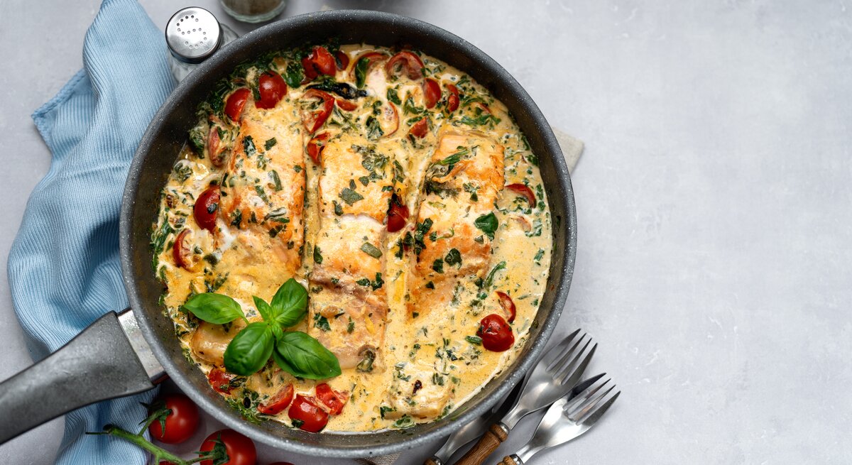 Draufsicht auf eine mediterrane Lachspfanne mit Tomaten & Spinat serviert in einer Pfanne. 