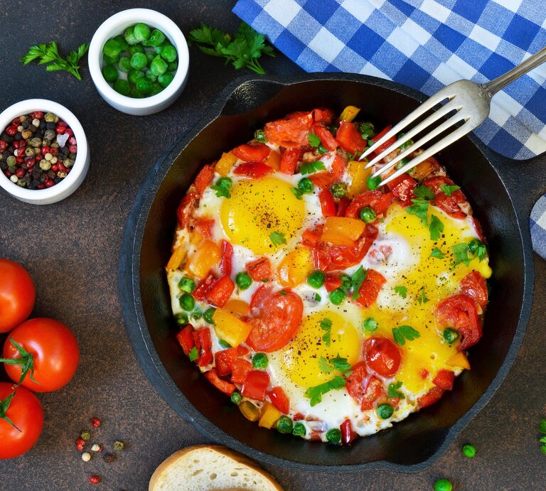 Draufsicht auf eine Eier-Tomaten-Pfanne garniert mit frischen Kräutern. | © iStock/zefirchik06