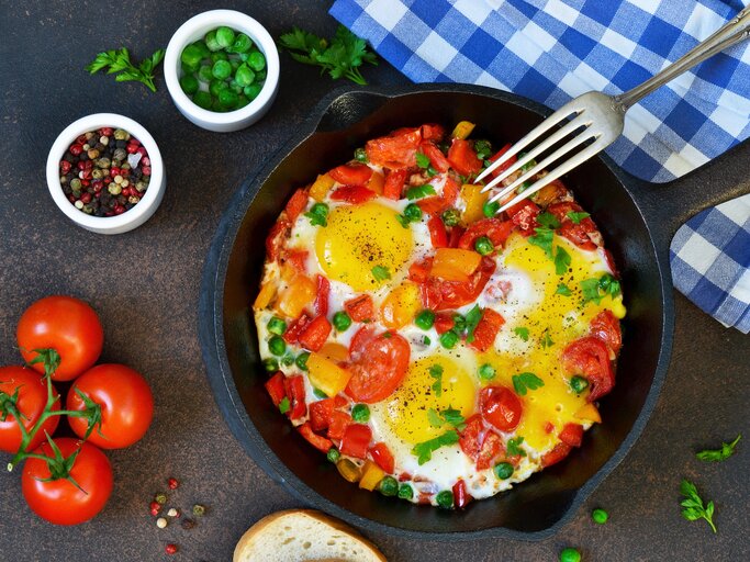 Draufsicht auf eine Eier-Tomaten-Pfanne garniert mit frischen Kräutern. | © iStock/zefirchik06