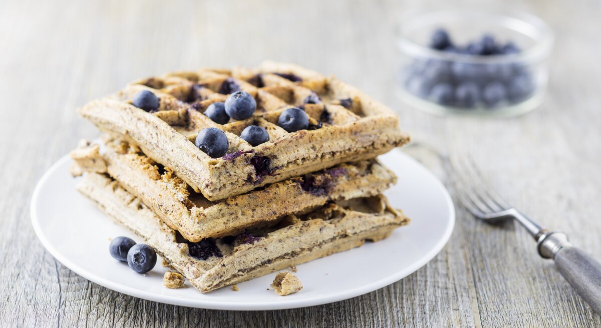 Mehrere Waffeln auf einem weißen Teller mit den Heidelbeeren von der Seite fotografiert.