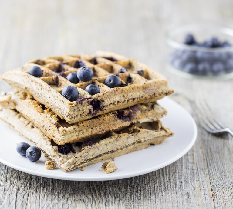 Mehrere Waffeln auf einem weißen Teller mit den Heidelbeeren von der Seite fotografiert. | © StockFood / Wischnewski, Jan
