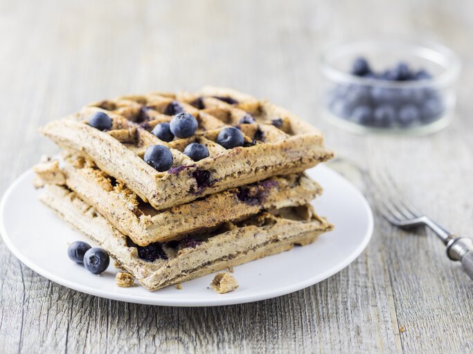 Mehrere Waffeln auf einem weißen Teller mit den Heidelbeeren von der Seite fotografiert. | © StockFood / Wischnewski, Jan