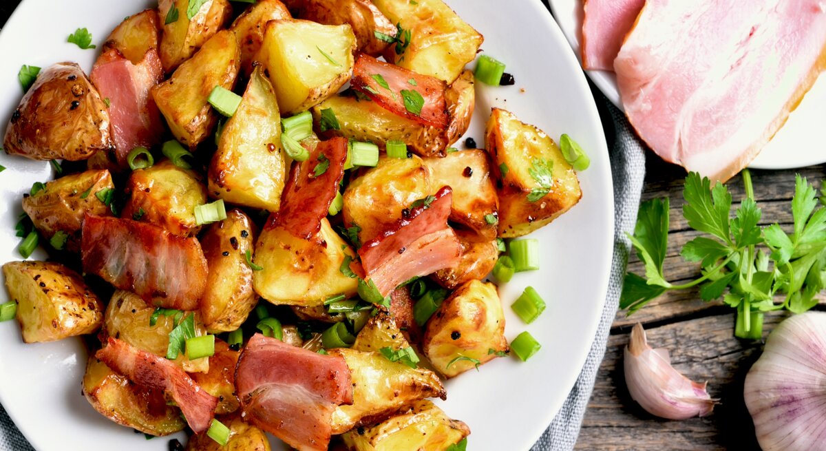 Ein Teller mit gebratenem Kohlrabi, Speckstreifen und frischen Frühlingszwiebeln, umgeben von frischen Kräutern.