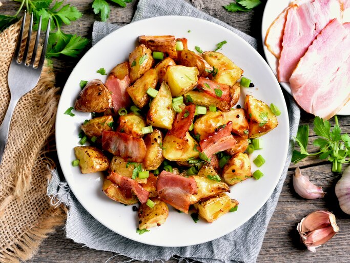 Ein Teller mit gebratenem Kohlrabi, Speckstreifen und frischen Frühlingszwiebeln, umgeben von frischen Kräutern. | © iStock/ Tatiana Volgutova