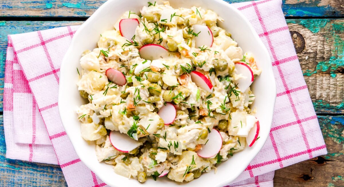 Falscher Kartoffelsalat mit Radieschen und Kräutern in weißer Schale auf rot-weißer Serviette, rustikaler Holztisch.
