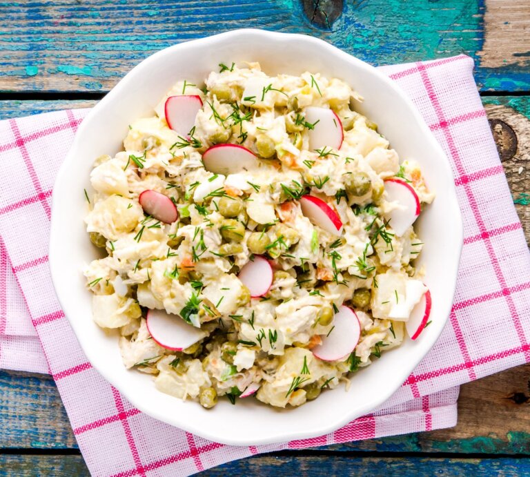 Falscher Kartoffelsalat mit Radieschen und Kräutern in weißer Schale auf rot-weißer Serviette, rustikaler Holztisch. | © iStock/wmaster890