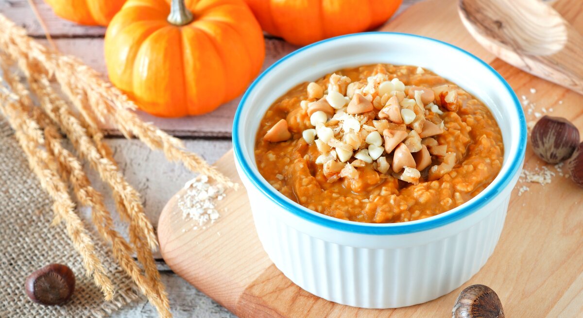 Eine weiß-blaue Schüssel mit Kürbis-Porridge auf einem Holzbrett.