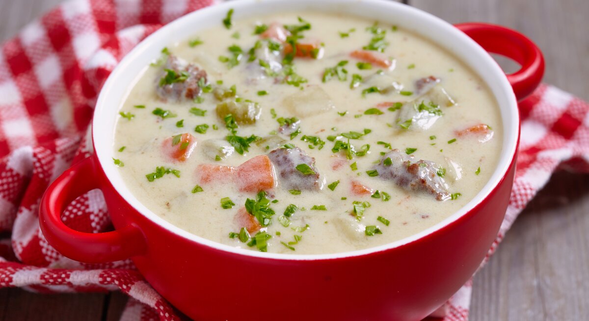 Roter Suppentopf gefüllt mit einer sahnigen Kohlrabisuppe mit Erbsen, Möhren und Hackfleisch. 