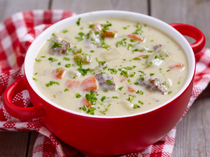 Roter Suppentopf gefüllt mit einer sahnigen Kohlrabisuppe mit Erbsen, Möhren und Hackfleisch.  | © iStock/Azurita