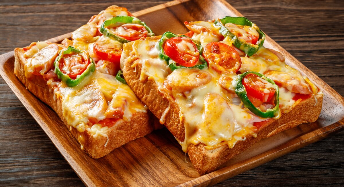 Überbackenes Toastbrot mit Tomaten und Würstchen auf Holzteller.