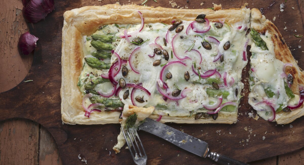 Ein dunkles Holzbrett mit der Tarte auf einem Holztisch direkt von oben fotografiert.