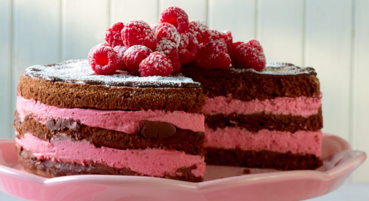 Schokoladentorte mit pinker Himbeercreme und frischen Früchten auf rosa Platte.