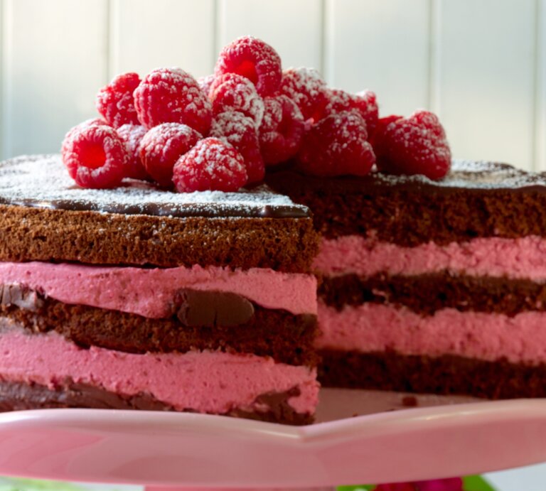 Schokoladentorte mit pinker Himbeercreme und frischen Früchten auf rosa Platte. | © Matthias Liebich