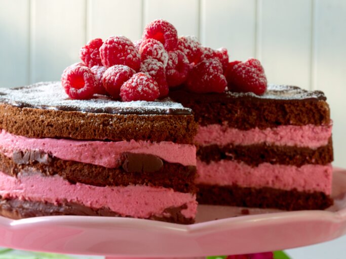 Schokoladentorte mit pinker Himbeercreme und frischen Früchten auf rosa Platte. | © Matthias Liebich