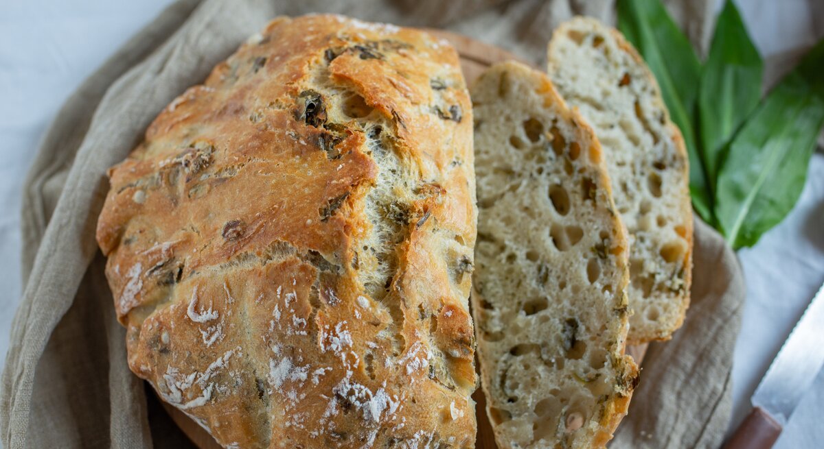 Bärlauchbrot mit Nüssen auf einem Geschirrtuch, daneben ein paar Bärlauchblätter.